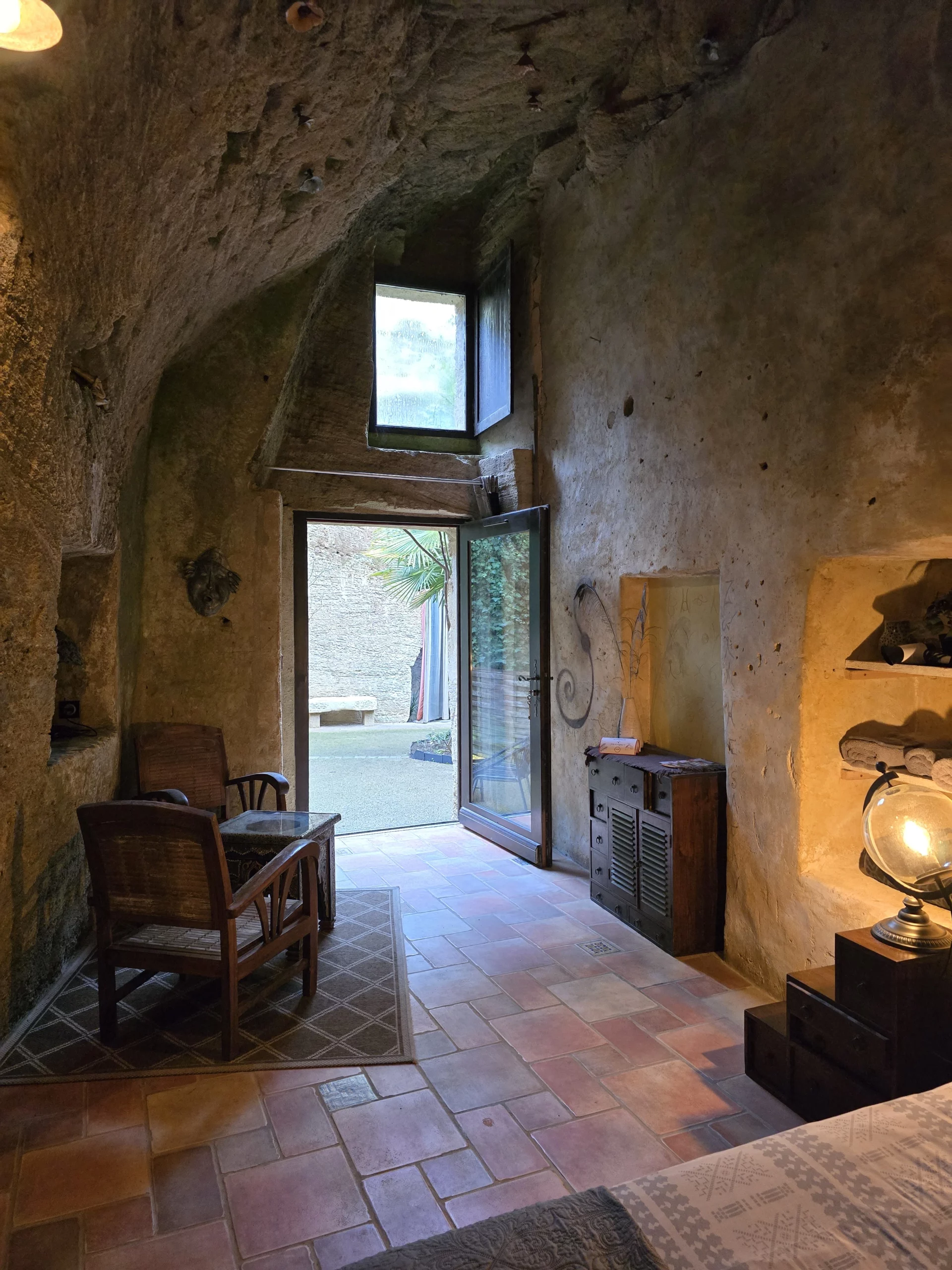Intérieur troglodytique authentique de la chambre Le Cocon aux Voûtes Oubliées, avec mobilier en bois, éclairage doux et vue sur cour