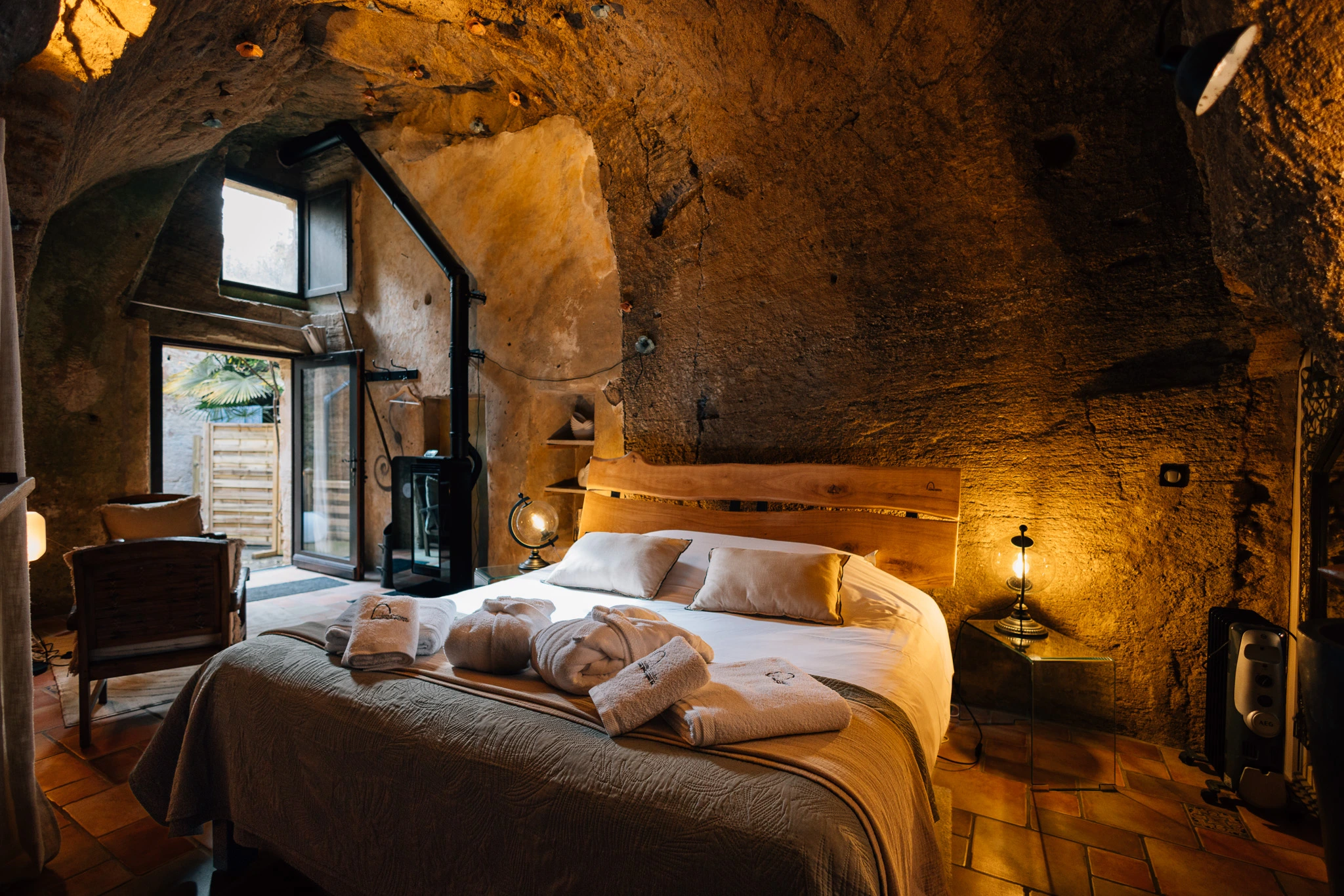 Intérieur troglodytique authentique de la chambre Le Cocon aux Voûtes Oubliées, avec mobilier en bois, éclairage doux et vue sur cour